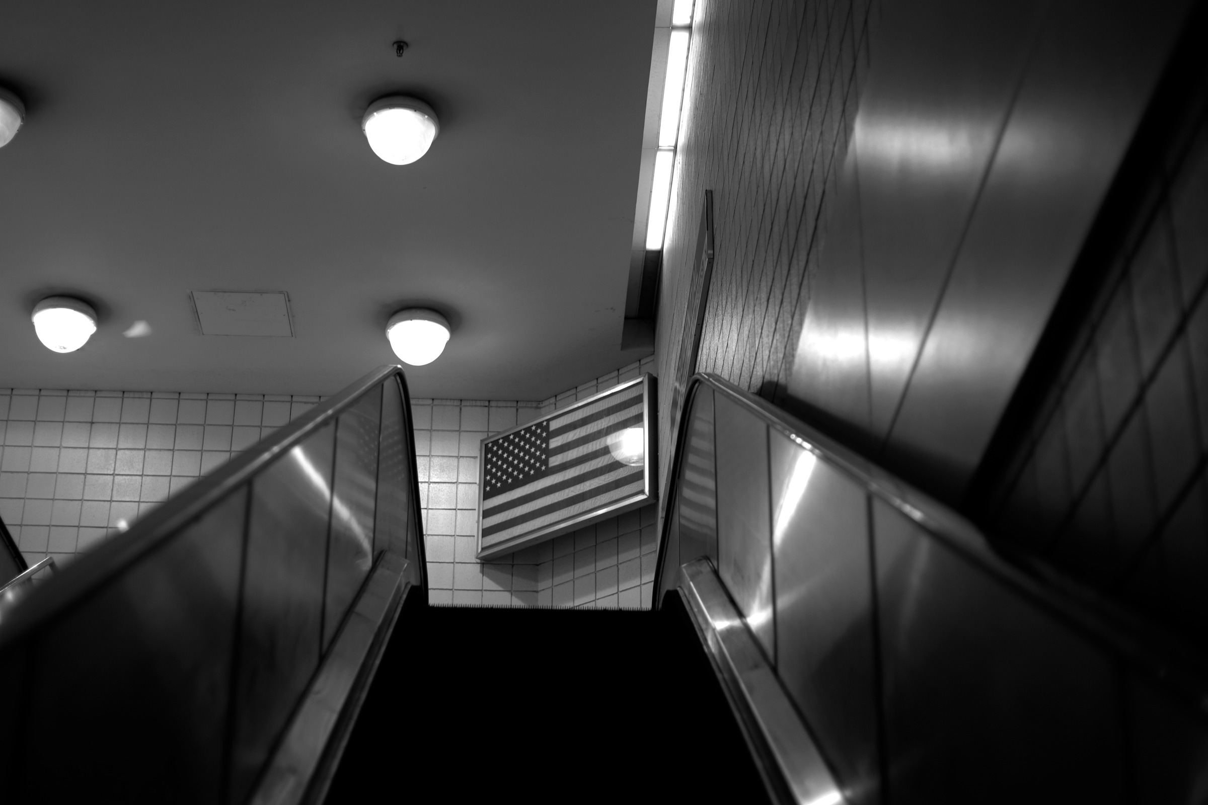 A stairway framed by tiled walls, handrails, and overhead lights.