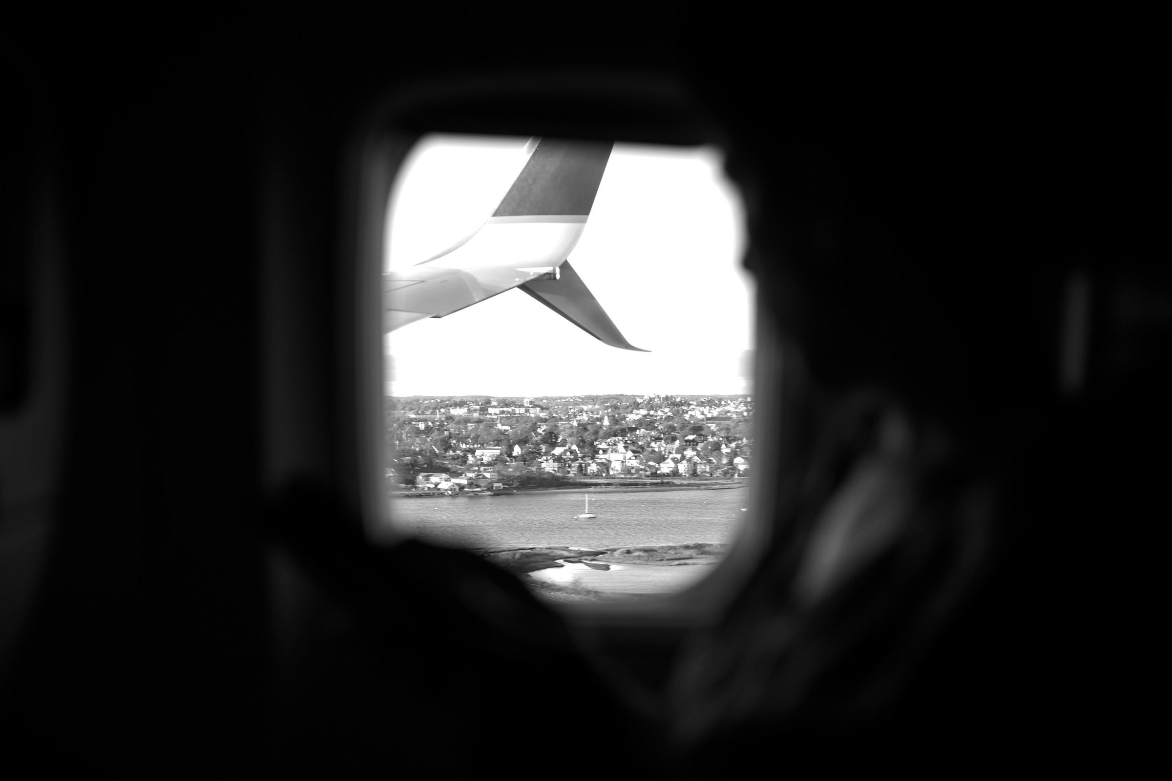 A view of an aircraft wing through a cabin window, framed by a passenger.