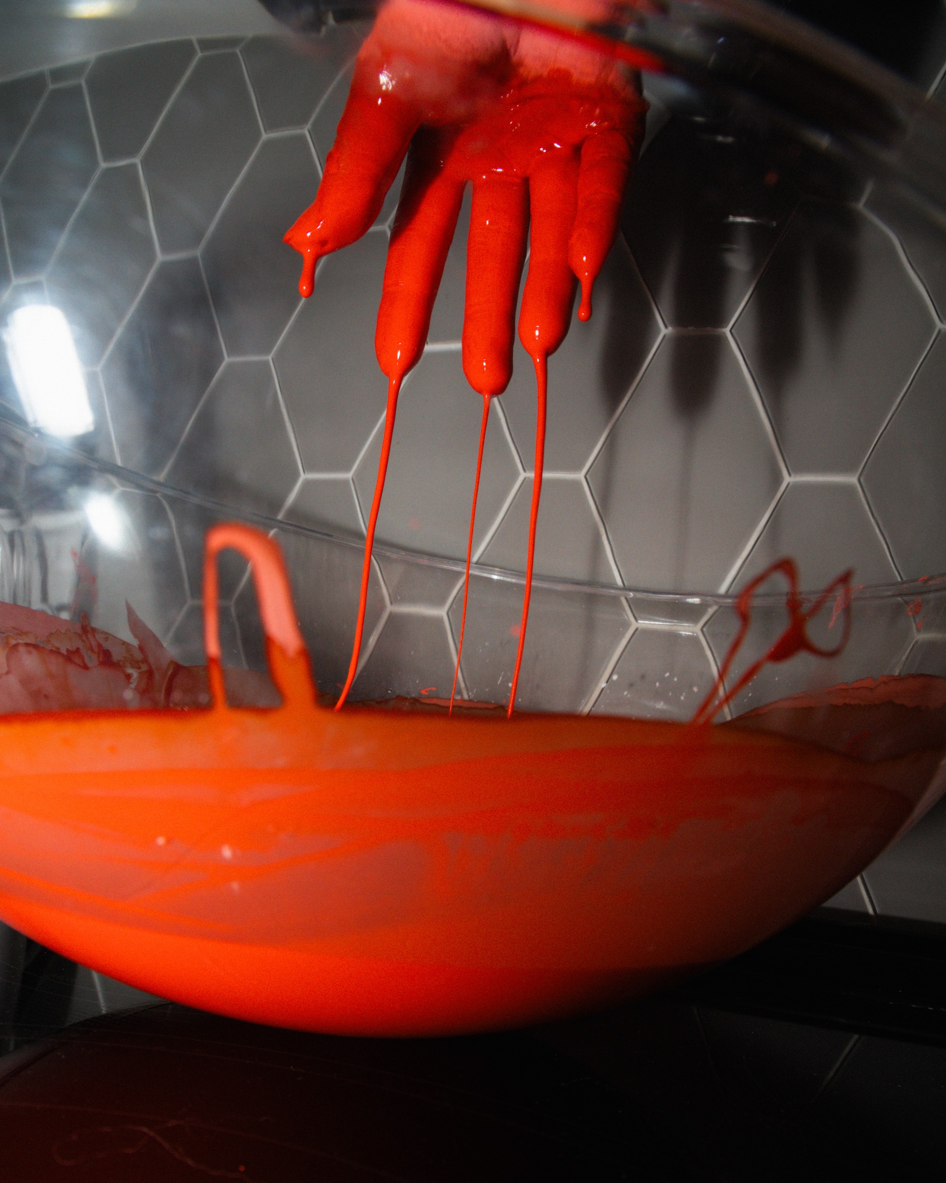 An orange hand form suspended above an orange bowl in a reflective setting.